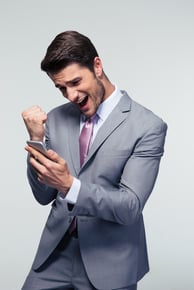 Happy businessman holding smartphone and celebrating his success over gray background.jpeg