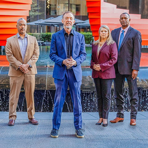 Chris Voss, Derek Gaunt, Sandy Hein, and Troy Smith standing in front of an outdoor fountain.